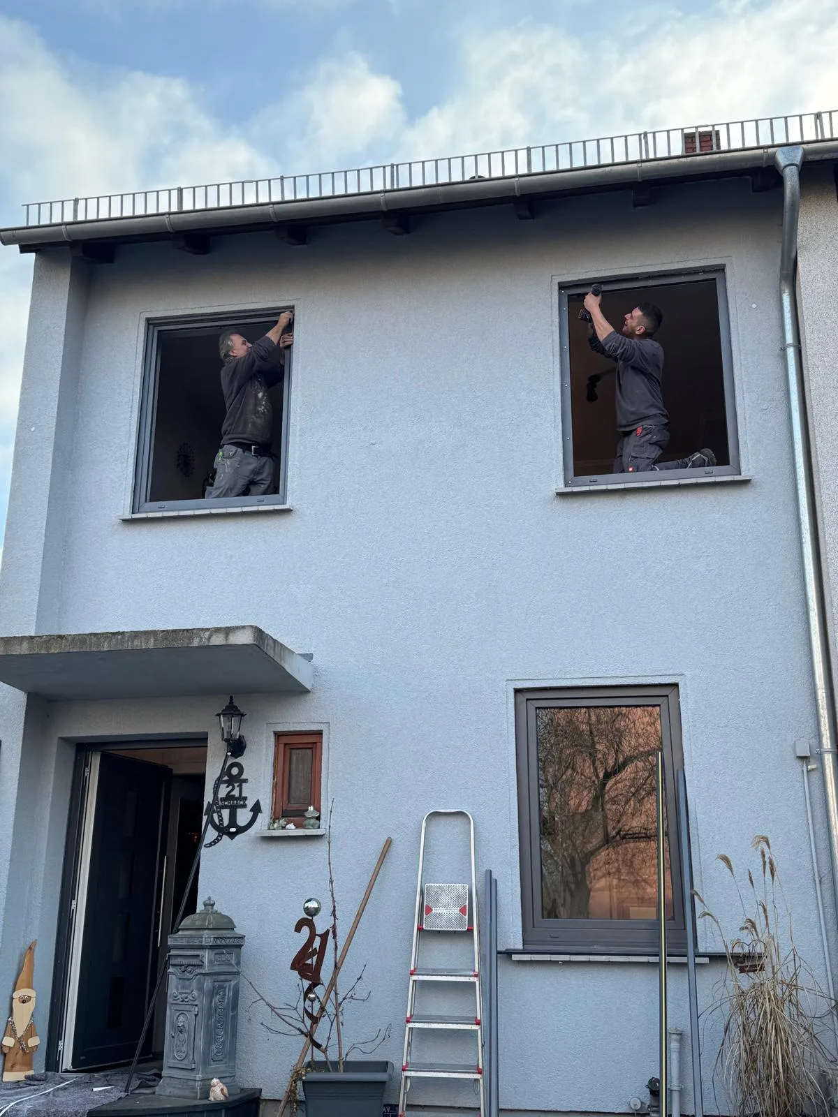 Zwei Handwerker montieren Fenster an einer hellblauen Hausfassade