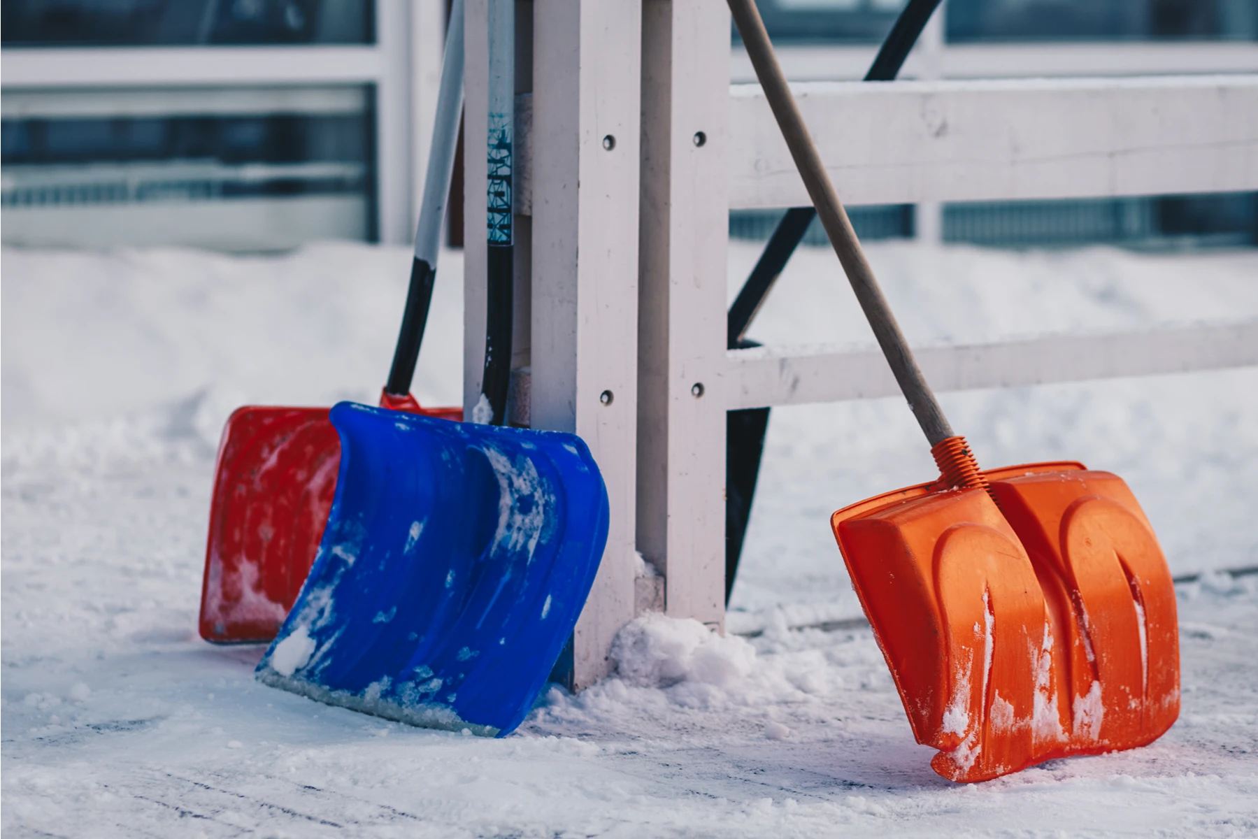 Zwei Schneeschaufeln in orange und blau stehen an einem weißen Pfosten im Schnee