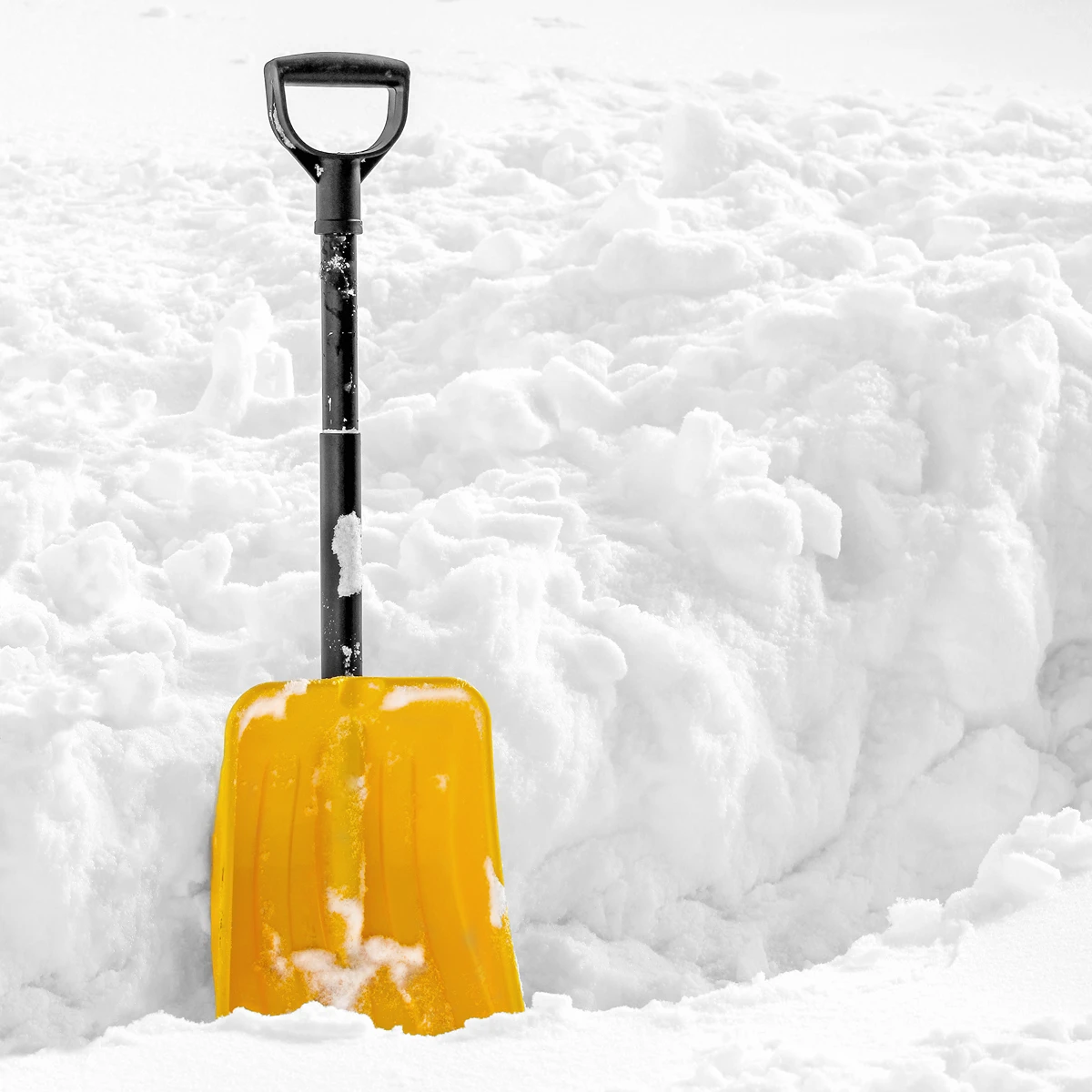 Gelbe Schneeschaufel steht im frisch gefallenen Schnee