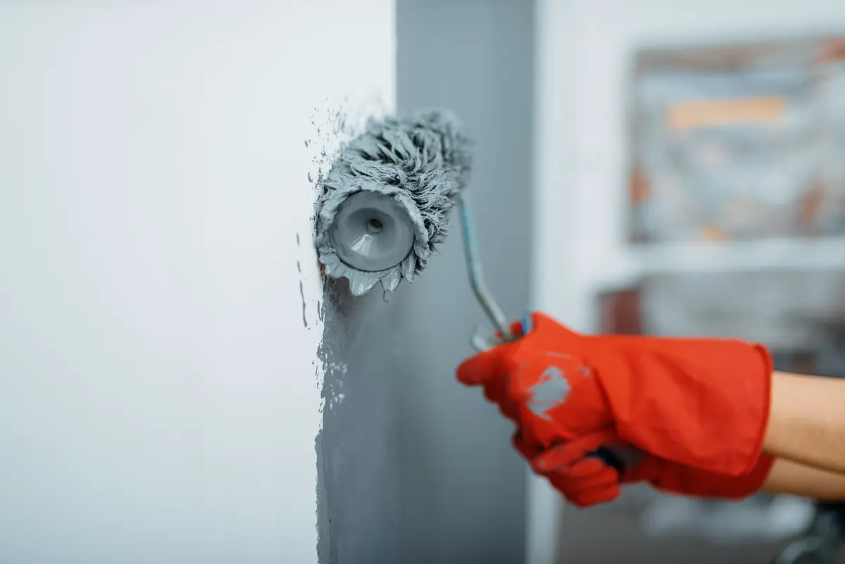 Ein Handwerker trägt graue Farbe mit einer Malerrolle auf eine Wand auf