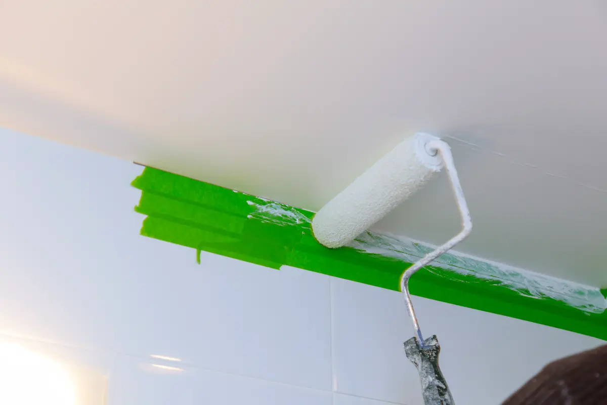 Malerarbeiten an der Decke mit grünem Abklebeband für präzise Kanten