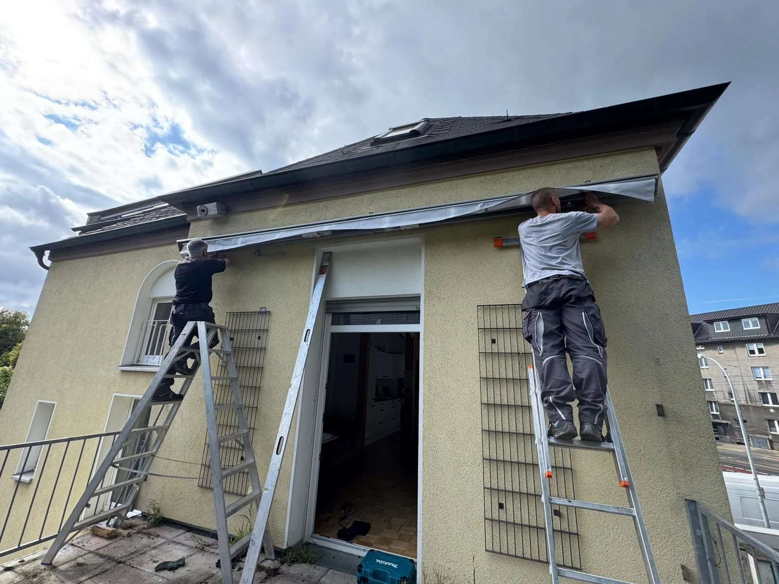 Zwei Handwerker montieren eine Terrassenüberdachung an einem Haus