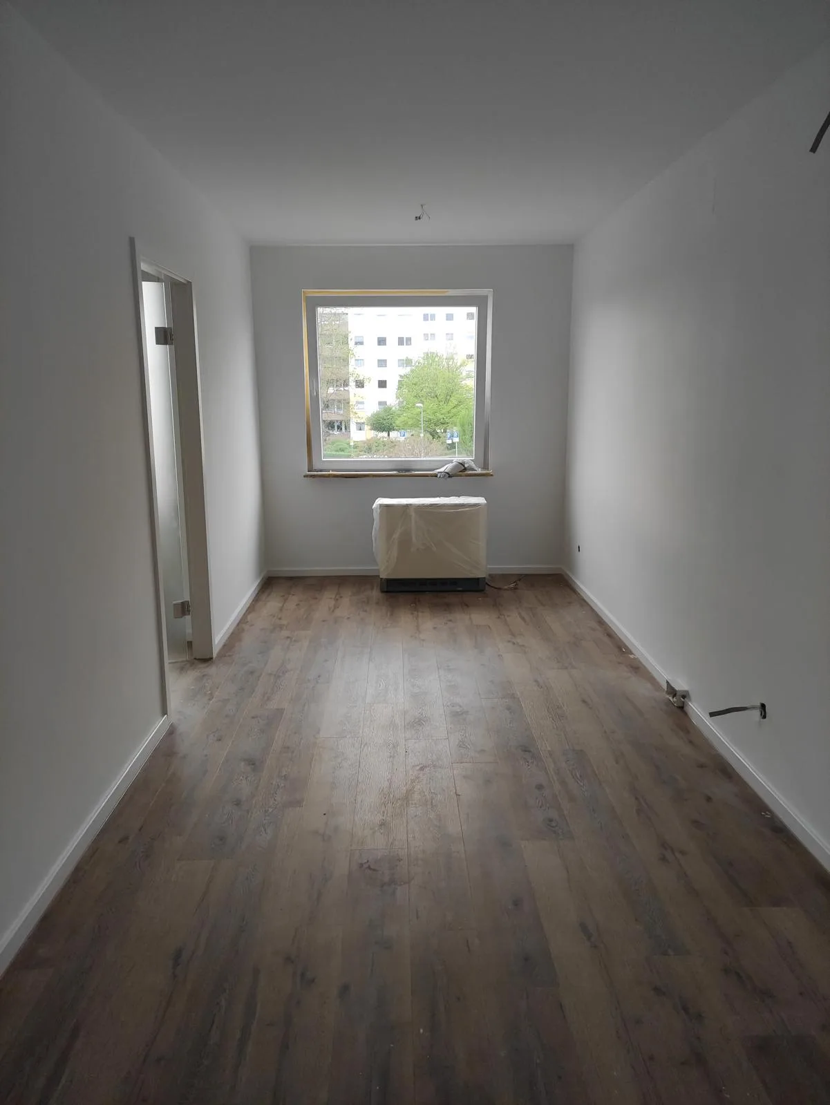 Leerer Raum mit Fenster und frisch verlegtem Fußboden, geeignet für Innenausbau