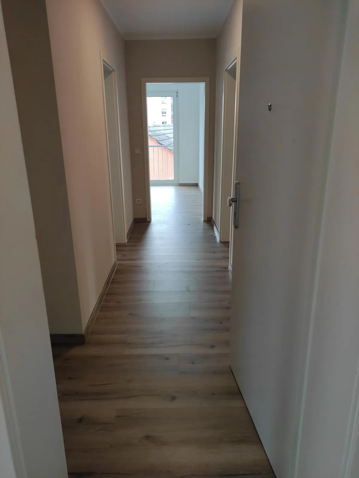 Flur mit hellen Wänden und Laminatboden, Sicht auf den Balkon
