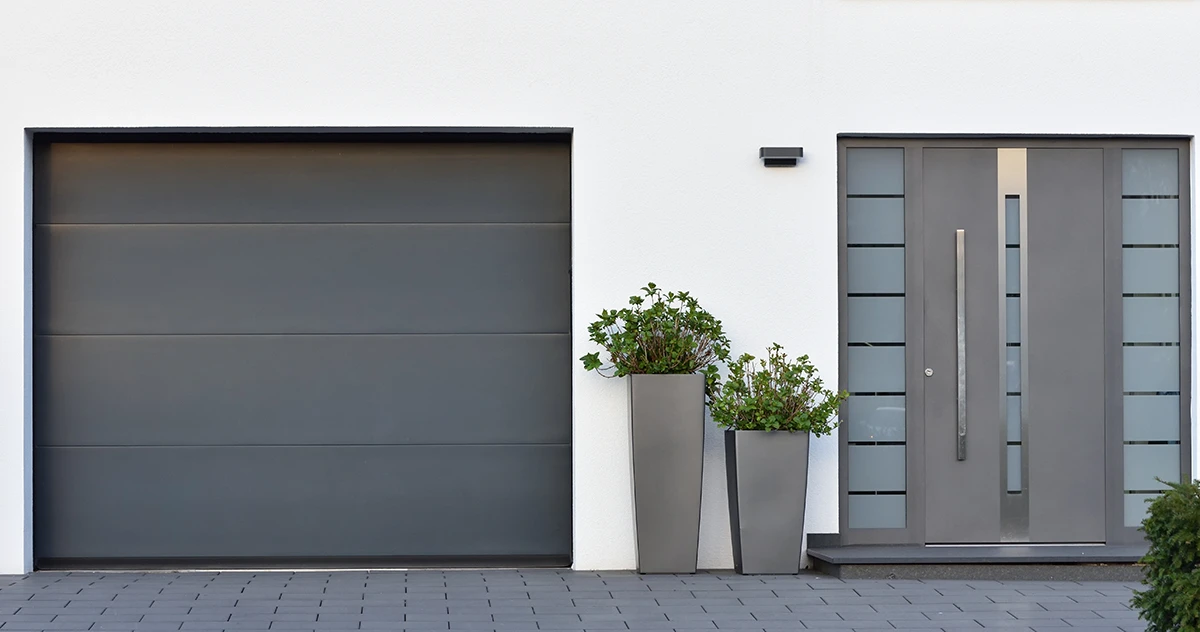 Moderne Haustür und Garagentor in neutralem Design, umgeben von Pflanzen