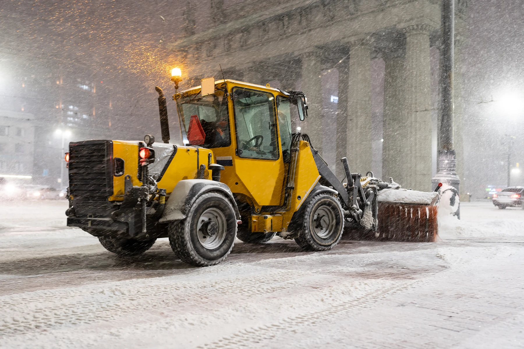 Schneeräumung mit einem gelben Schnee-Räumfahrzeug bei Nacht in der Stadt